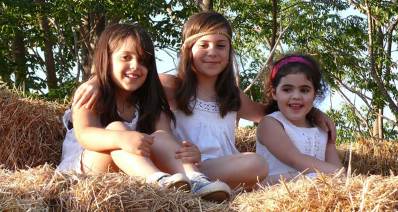 שלוש ילדות בלבוש בלבוש לחג השבועות על ערימות חציר