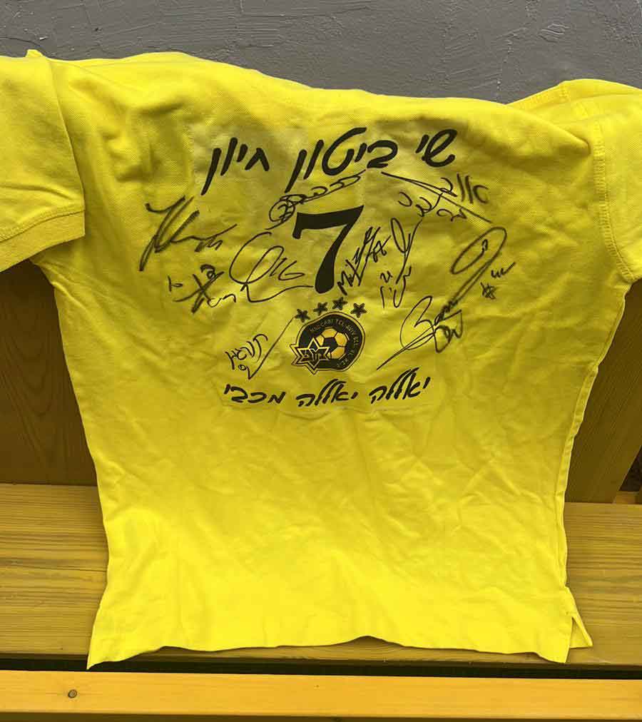 חולצה צהובה שי ביטון חיון מספר 7. עם סמל מכבי תל אביב כדורגל וחתימות השחקנים. כיתוב על החולצה יאללה יאללה מכבי