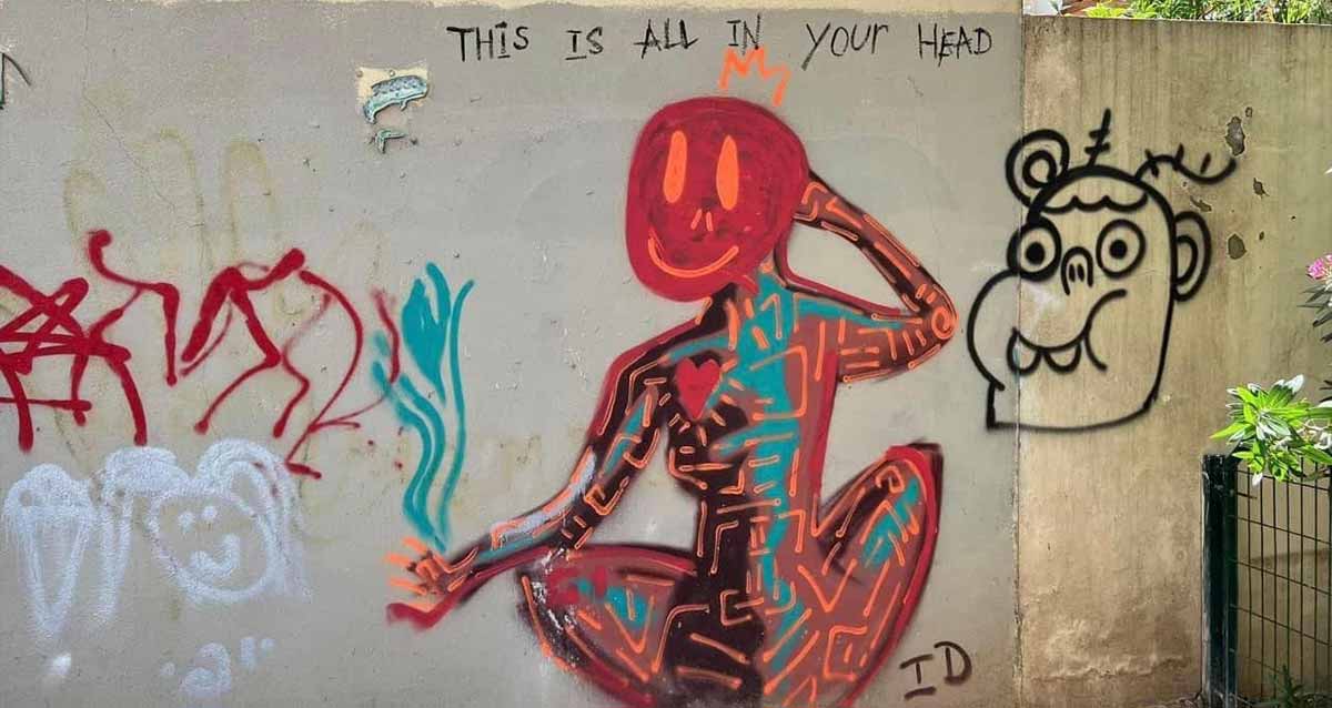 גרפיטי צבעוני, ציור בצבעים אדום, כתום, שחור, וכחול של אישה יושבת, מיד ימין עולה להבה בצבע כחול ויד שמאל בראשה. מימין לאישה ציור של ראש גבר בצבע שחור. משמאל לאישה קשקוש בצבע אדום ומתחתיו ראש אישה בצבע לבן ומתחתיו כתוב בלבן: יופי