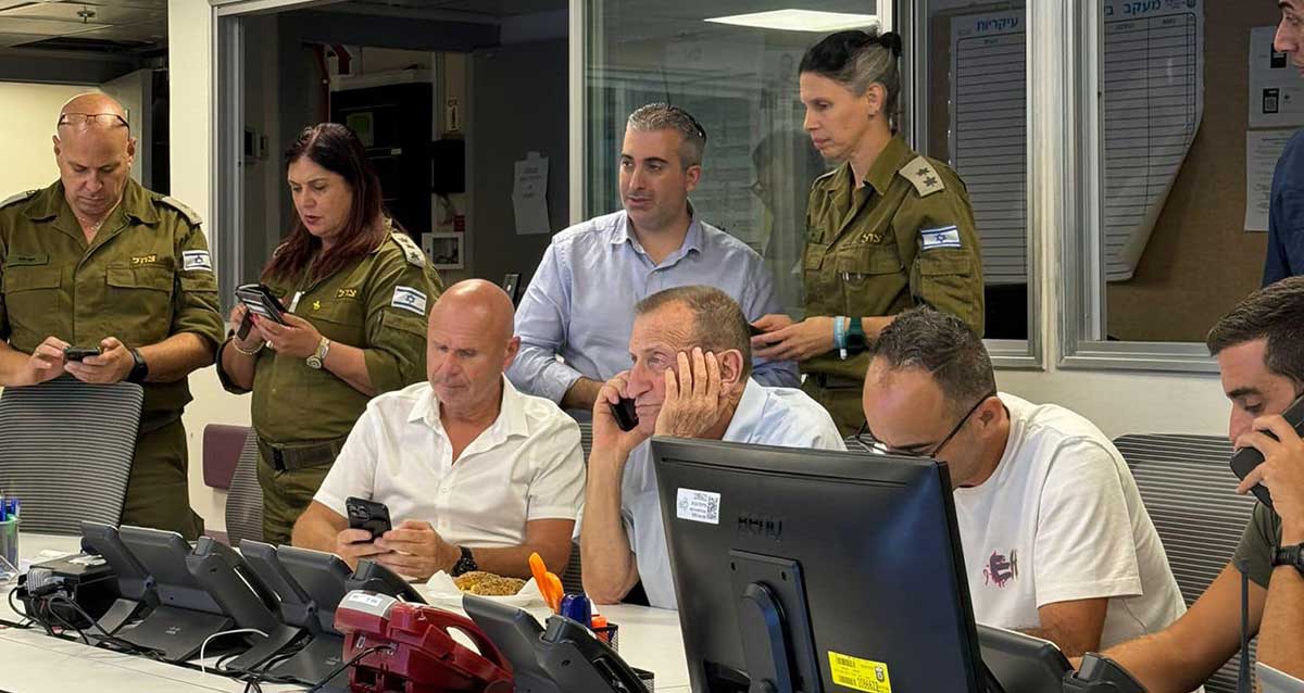 חמ"ל החירום בתל אביב במתקפת הטילים האיראנית. ליד שולחן עם מחשבים וטלפונים יושב ראש העיר רון חולדאי וחברי מטה החירום. מאחוריהם עומדים קצינים וחבר מטה החירום עם טלפונים ביד. מול חולדאי על השולחן הטלפון האדום..