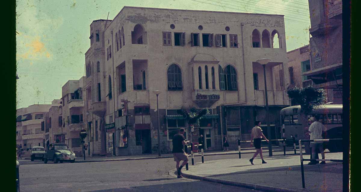 בית אוסישקין בפינת רחובות אלנבי והירקון בשנת 1963. בניין בן שלש קומות. חלונות מעוגלים בחלק העליון בקומה השנייה. הולכי רגל במדרכה בצד ימין.